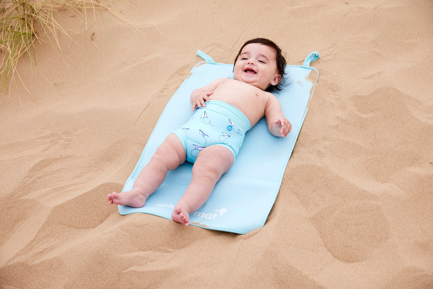 Junge liegt am Strand mit der Schwimmwindel "Paper Planes"