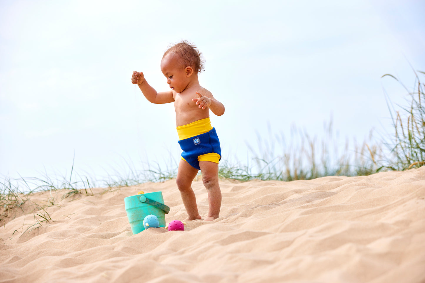 Kind mit Schwimmwindel "blue + yellow" am Strand