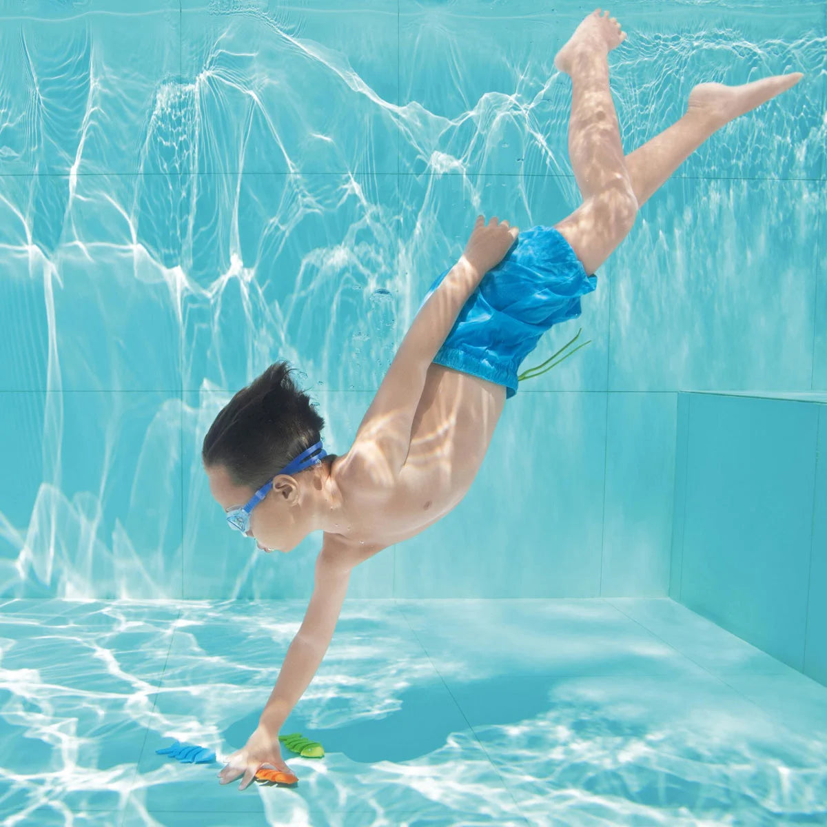 Junge holt "Squiggle Wiggle" Tauchfische vom Boden des Schwimmbeckens