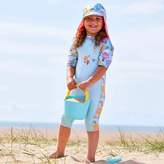 Mädchen trägt UV Schwimmanzug "Up And Away" und Sonnenhut am Strand