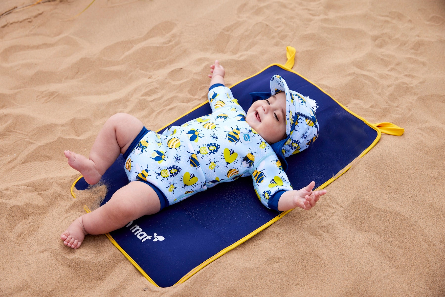 Baby trägt Neopren-Wetsuit und UV Sonnenhut und liegt auf der antibakteriellen Wickelunterlage