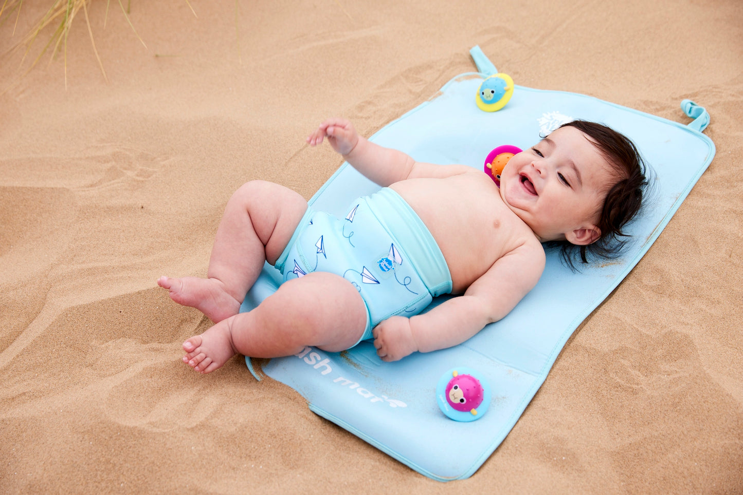 Junge am Strand liegt auf der antibakteriellen Wickelunterlage mit der Schwimmwindel "Paper Planes"
